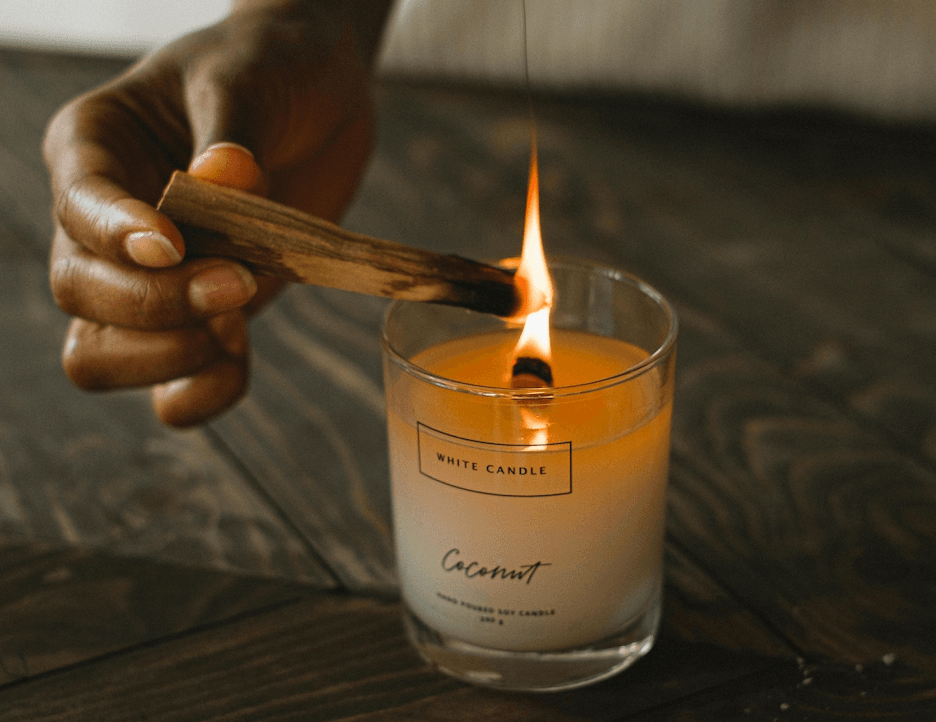 Hand lighting a Palo Santo stick with a candle, creating a sensory anchor for a mindful microdosing practice.