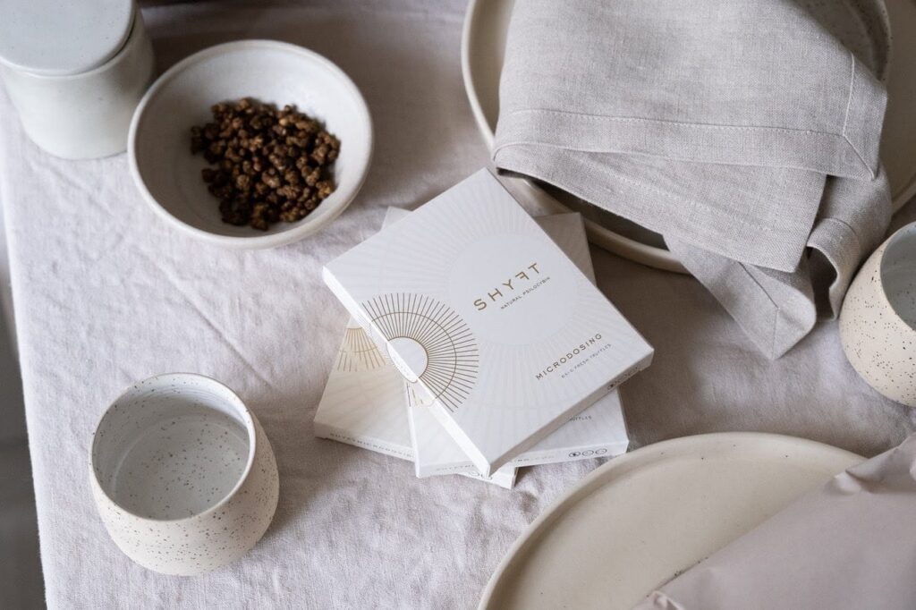 Twee pakjes truffels van het merk SHYFT met daarnaast een kopje koffie en een schaaltje. Het lijkt op een ontbijt met truffels.